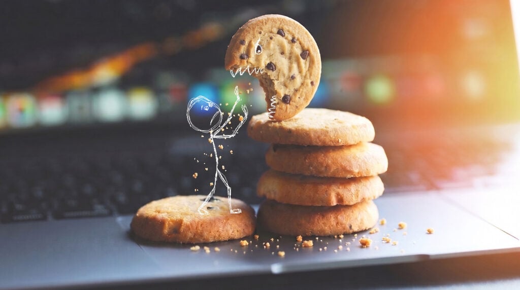 Drawn stick figure getting attacked by a chocolate chip cookie with drawn monster teeth on a laptop keyboard.